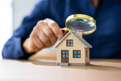 A man looks at a miniature house with a magnifying glass.